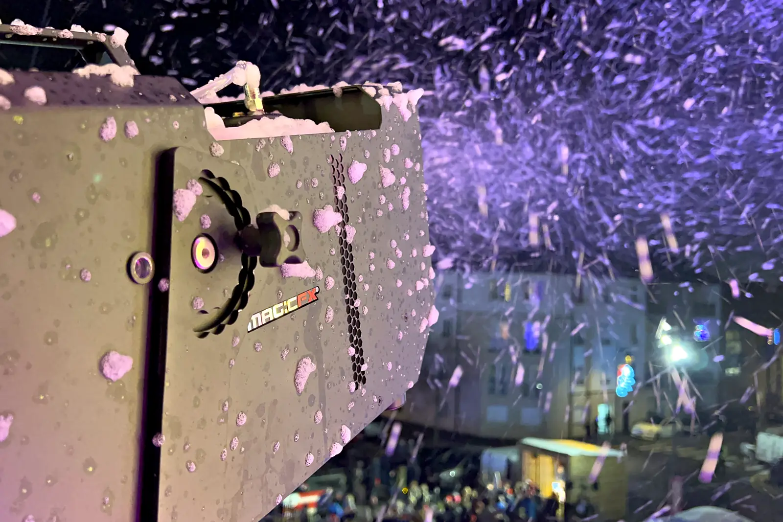 Machine à neige professionnelle en fonctionnement, buse couverte de flocons, au-dessus du public d’une animation de Noël