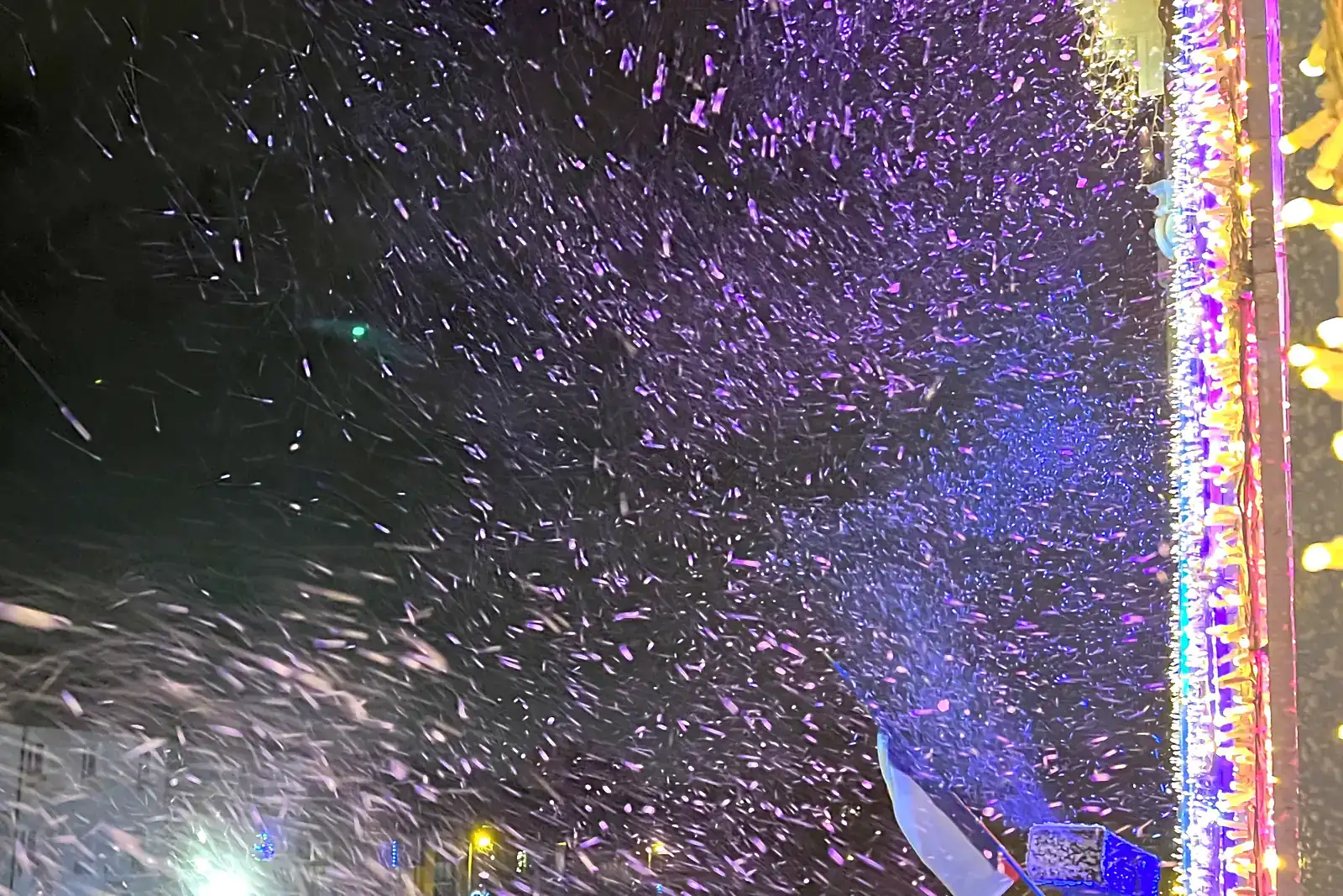 Rideau de flocons de neige artificielle tombant la nuit sur des décorations lumineuses de Noël