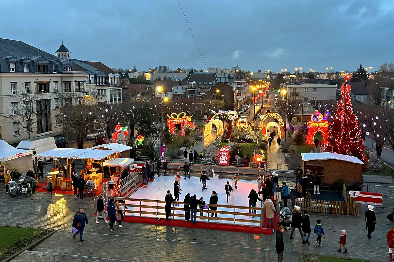 Village de Noël avec patinoire et chalets illuminés sous une neige artificielle produite par une machine à neige